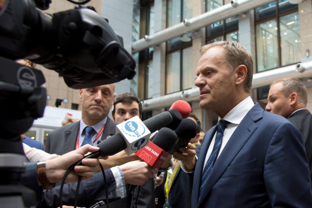 Tusk - wearing a navy suit and tie - has a number of microphones and cameras pointing at him.