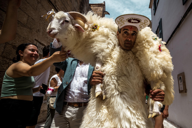 ciutadella-spain-18th-june-2023-a-young-man-clad-in-a-sheepskin-the-shomo-des-be-sheepman-carries-a-live-ram-around-his-shoulders-as-he-spends-the-sunday-before-ciutadellas-saint-john-fest
