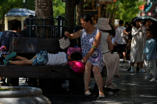 a-woman-uses-a-fan-to-cool-a-child-as-they-sit-on-a-bench-at-qianmen-pedestrian-shopping-street-on-a-hot-day-in-beijing-thursday-june-29-2023-the-entire-planet-sweltered-for-the-two-unofficial-hot