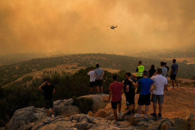 a-firefighting-helicopter-flies-through-smoke-as-people-look-on-in-mandra-west-of-athens-on-tuesday-july-18-2023-in-greece-where-a-second-heatwave-is-expected-to-hit-thursday-three-large-wildfir