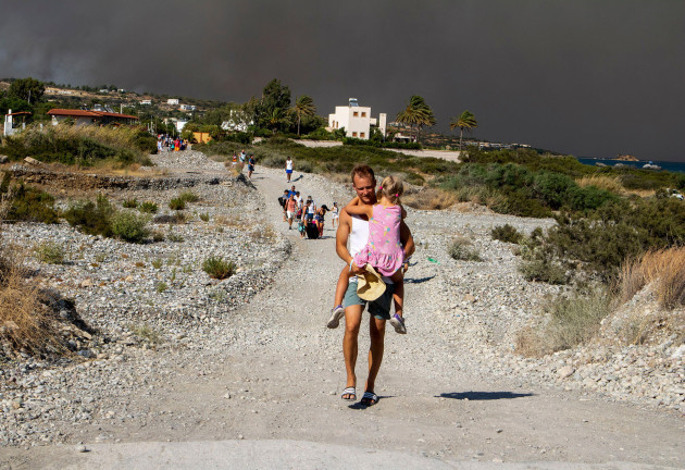 a-man-carries-a-child-as-they-leave-an-area-where-a-forest-fire-burns-on-the-island-of-rhodes-greece-saturday-july-22-2023-a-large-wildfire-burning-on-the-greek-island-of-rhodes-for-a-fifth-day