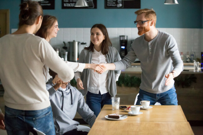 millennialguyhandshakingsmilinggirlintroducinggreetingatgroupmeeting