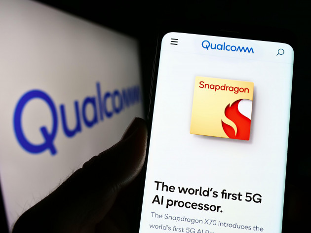 person-holding-cellphone-with-webpage-of-us-semiconductor-company-qualcomm-incorporated-on-screen-with-logo-focus-on-center-of-phone-display