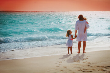 motherwithlittlegirlslookingatsunsetontropicalbeach