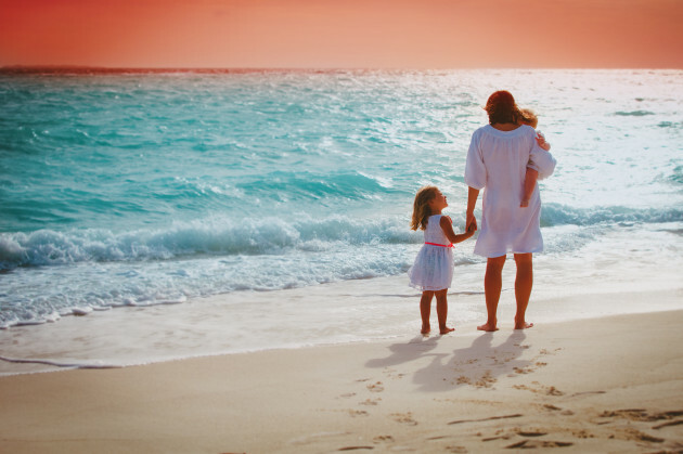 motherwithlittlegirlslookingatsunsetontropicalbeach