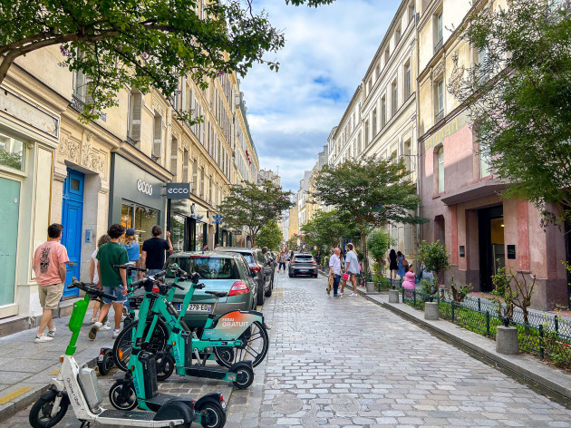 paris-france-small-crowd-of-people-tourists-walking-street-scene-visiting-le-marais-historic-neighborhood-electric-scooters