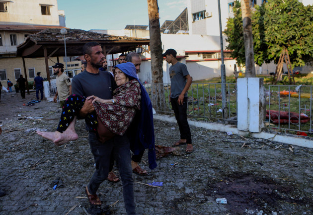 a-palestinian-man-carries-an-elderly-woman-past-the-site-of-a-deadly-explosion-at-al-ahli-hospital-in-gaza-city-wednesday-oct-18-2023-the-hamas-run-health-ministry-says-an-israeli-airstrike-caus