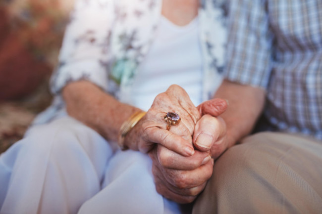 cropped-shot-of-elderly-couple-holding-hands-while-sitting-together-at-home-focus-on-hands