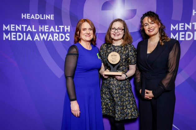 Maria holding the wooden award wearing a black and gold dress, with Nicola and Áine on either side.