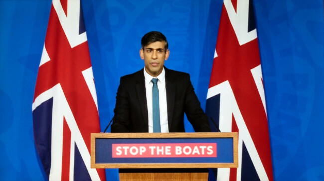 prime-minister-rishi-sunak-standing-at-podium-with-stop-the-boats-sign-flanked-by-union-jack-flags-speaking-15-november-2023-london-uk