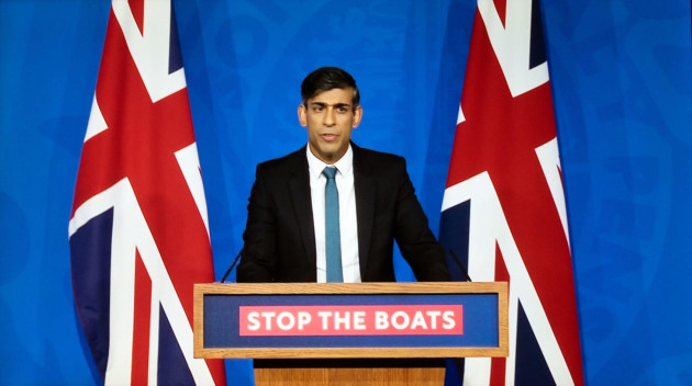 prime-minister-rishi-sunak-standing-at-podium-with-stop-the-boats-sign-flanked-by-union-jack-flags-speaking-15-november-2023-london-uk