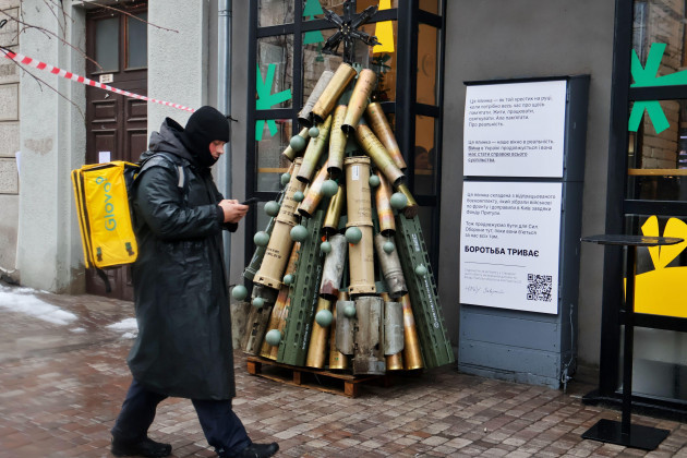 kyiv-ukraine-december-17-2023-a-food-delivery-courier-walks-past-an-installation-in-the-form-of-a-christmas-tree-made-of-fired-shells-and-anti-tank-grenade-launchers-on-december-17-2023-in-kyiv