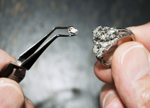 Hand holding a diamond ring with gemstones in tweezers