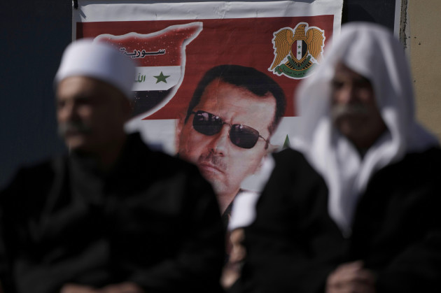 druze-men-sit-in-front-of-a-poster-of-syrian-president-bashar-assad-during-a-rally-calling-for-the-return-to-syria-of-the-golan-heights-captured-by-israel-in-1967-in-majdal-shams-in-the-israeli-cont
