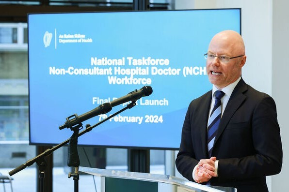Stephen Donnelly wearing a suit and standing at a podium with a screen behind saying: Department of Health, National Taskforce Non-Consultant Hospital Doctor (NCHD) Workforce, Final Report Launch, 7th February 2024.