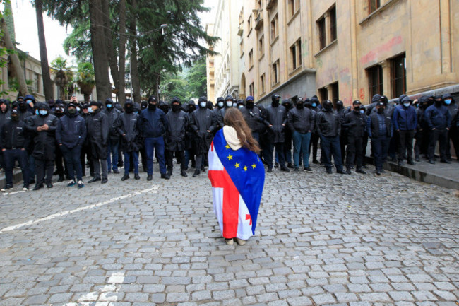 a-demonstrator-with-draped-georgian-national-and-eu-flags-stands-in-font-of-police-blocking-the-way-to-the-parliament-building-during-an-opposition-protest-against-the-russian-law-in-the-center-of