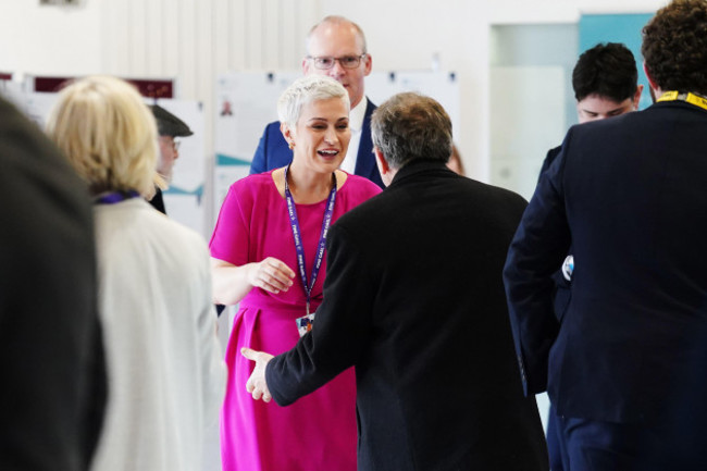 Maria Walsh, wearing a pink dress, speaking to people at a conference.