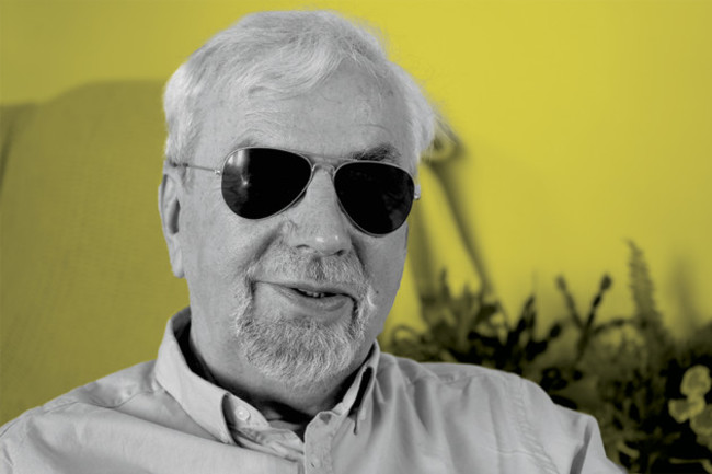 Des Kenny wearing sunglasses and a shirt, with a plant in the background.