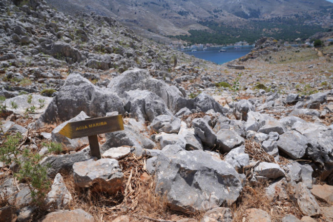 a-direction-sign-on-a-rocky-path-in-the-hills-of-pedi-pedi-centre-pictured-in-the-distance-right-a-small-fishing-village-in-symi-greece-pointing-toward-agia-marina-where-the-body-of-tv-doctor-a