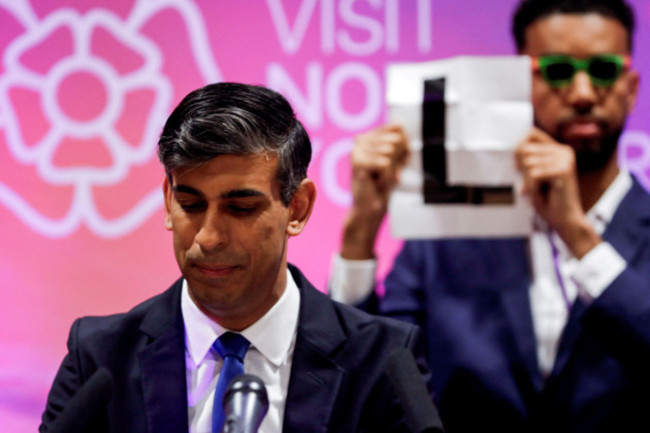 independent-candidate-niko-omilana-holds-an-l-behind-prime-minister-rishi-sunak-during-his-speech-at-northallerton-leisure-centre-in-northallerton-north-yorkshire-after-holding-his-seat-in-the-ric