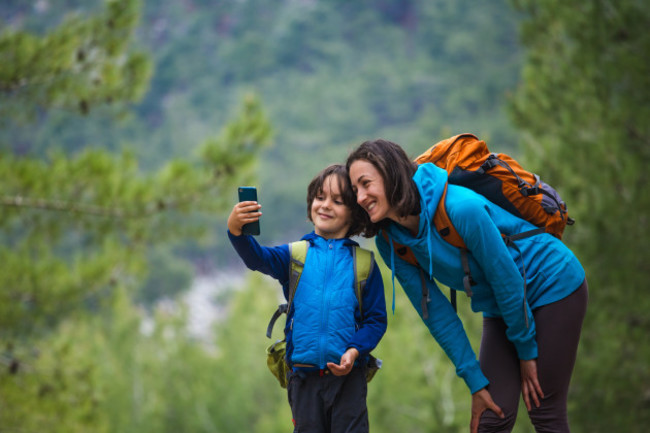 a-child-with-a-backpack-takes-a-selfie-on-a-smartphone-with-mom-on-the-background-of-a-mountain-forest