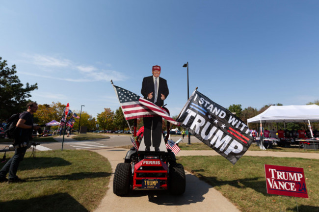 saginaw-usa-03rd-oct-2024-a-trump-supporter-drives-a-riding-lawn-mower-adorned-with-flags-and-a-cardboard-cutout-of-trump-around-the-parking-lot-and-vendor-area-outside-of-the-former-presidents