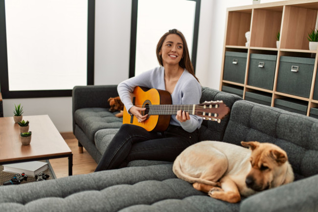 younghispanicwomanplayingclassicalguitarsittingonsofawith