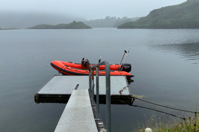 A small red motorised boat tied up on a wooden mooring on the lough.
