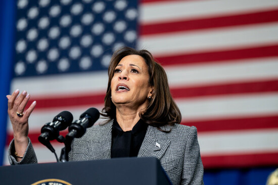 vice-president-kamala-harris-gives-a-speech-while-gesturing-with-her-right-hand-standing-at-a-podium-in-front-of-an-american-flag-in-the-background