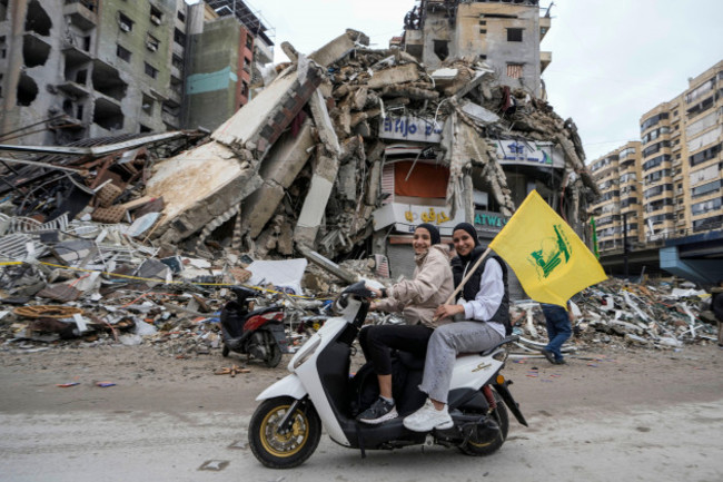 women-on-a-scooter-hold-a-hezbollah-flag-as-they-drive-past-a-destroyed-building-in-dahiyeh-in-beirut-lebanon-following-a-ceasefire-between-israel-and-hezbollah-that-went-into-effect-on-wednesday