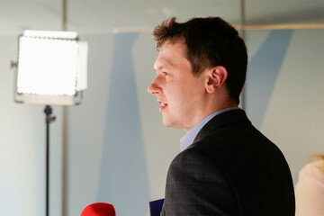 Harris wearing a shirt and suit jacket speaking beside a microphone with a light behind him.