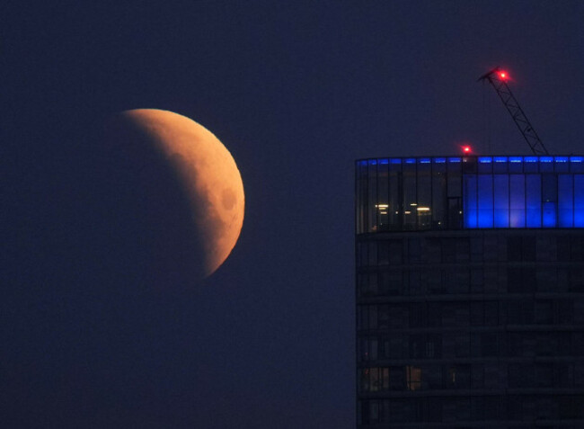 a-lunar-eclipse-is-visible-above-canary-wharf-in-london-as-the-full-moon-passes-into-earths-shadow-unlike-in-other-parts-of-the-world-except-for-some-extreme-western-areas-of-the-uk-the-eclipse-wi