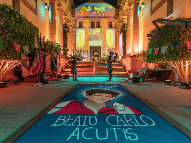 aztec-dancers-stand-by-a-traditional-sawdust-carpet-or-tapete-with-the-image-of-blessed-carlo-acutis-an-english-born-italian-15-year-old-student-who-as-an-amateur-computer-programmer-documented-an