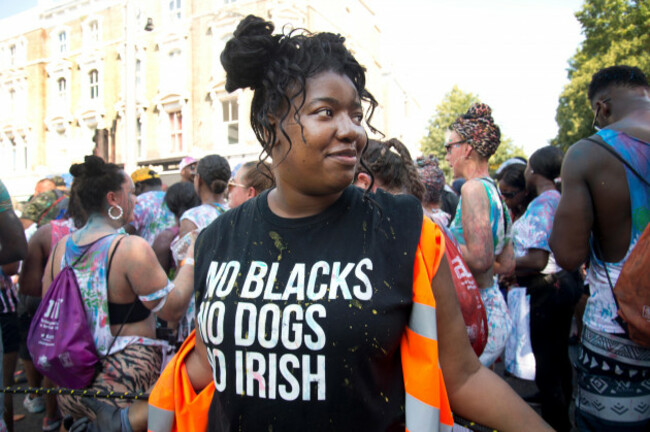 notting-hill-carnival-august-25th-2019-a-black-woman-wears-a-t-shirt-saying-no-blacks-no-dogs-no-irish-refering-to-notices-advertsing-rooms-to