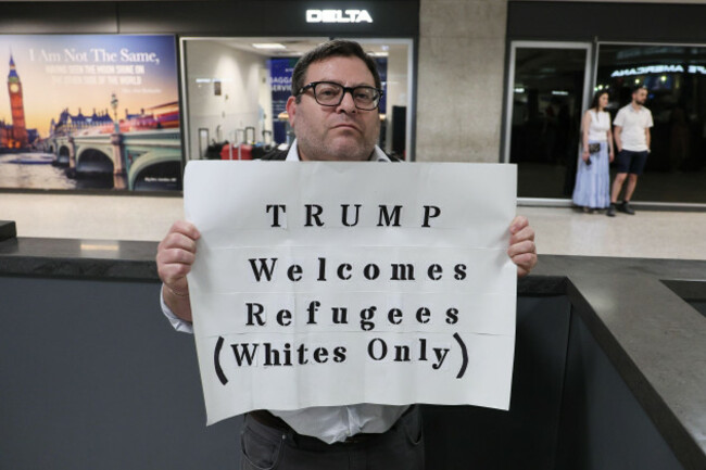 a-protestor-holds-up-a-sign-protesting-president-trumps-new-policies-towards-refugees-at-the-international-arrivals-terminal-at-dulles-international-airport-as-the-first-flight-of-afrikaners-from-sout
