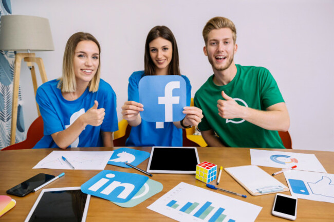 smiling-woman-holding-facebook-logo-with-his-friends-showing-thumbup-sign