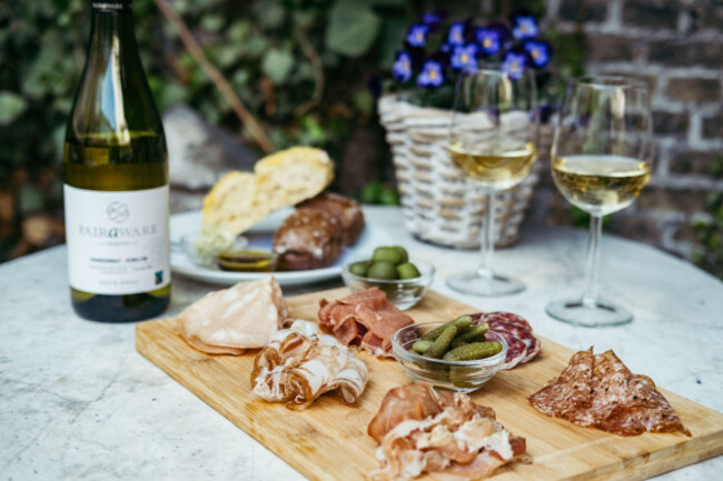 two-glasses-and-bottle-of-white-wine-with-gourmet-charcuterie-board-on-round-marble-table-garden-party
