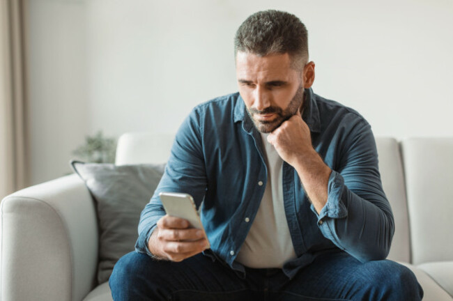 thoughtful-middle-aged-man-doom-scrolls-through-phone-at-home