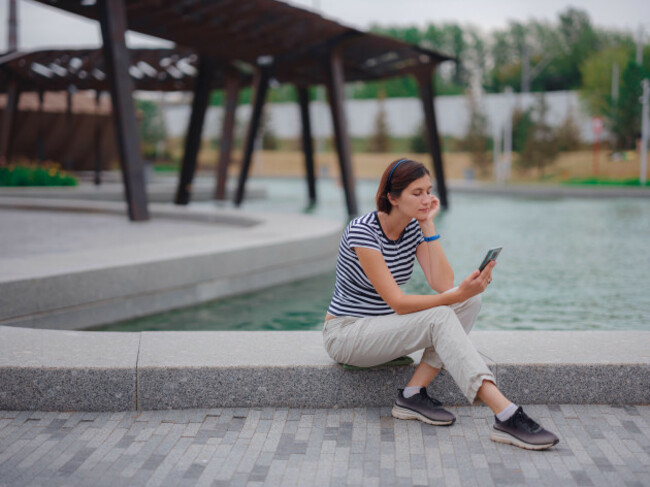 young-femle-hipster-chatting-on-cell-phone-online-with-her-friends-and-listening-to-music-pretty-woman-reading-text-message-on-her-cell-phone-while-r