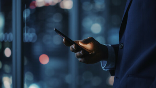 nightofficesuccessfulblackbusinessmanwearingsuitstandingusingsmartphone