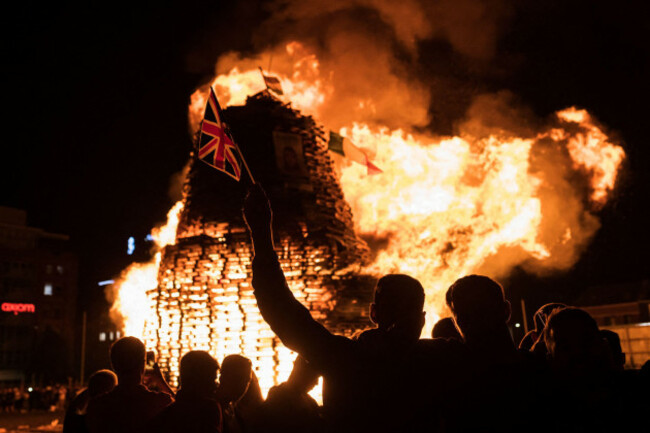 a-man-waves-a-union-jack-flag-in-front-of-the-burning-bonfire-set-on-sandy-row-area-in-belfast-on-the-day-before-the-orange-day-its-a-tradition-to-burn-these-heavy-constructions-all-around-northern