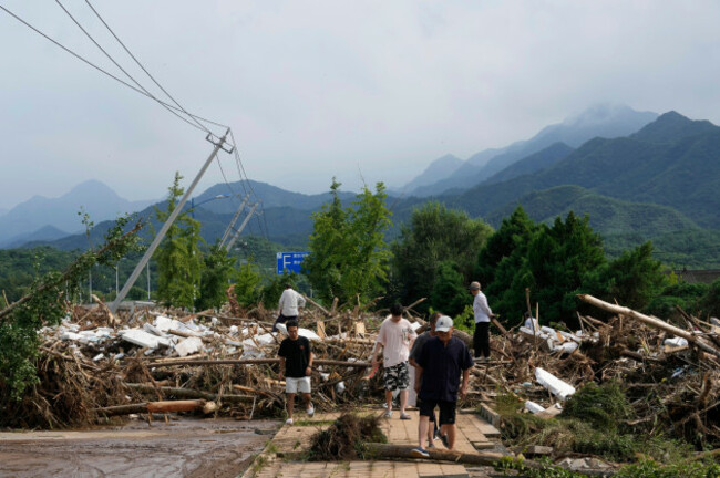local-residents-walks-in-front-of-a-damaged-road-littered-with-broken-tree-branches-after-a-heavy-rains-in-taishitun-town-miyun-district-on-the-outskirts-of-beijing-china-monday-july-28-2025-ap