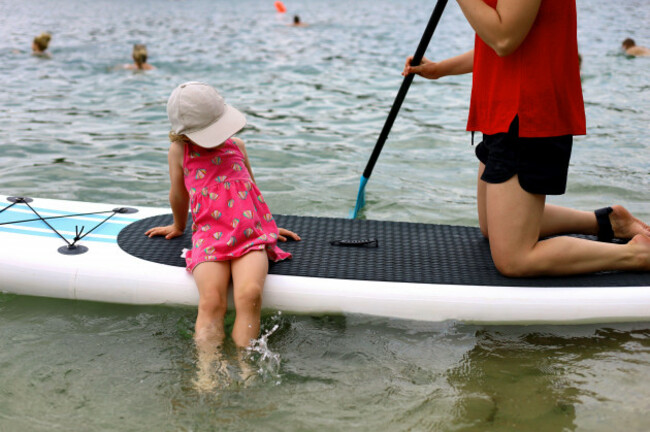 little-girl-in-pink-summer-dress-and-a-hat-sitting-on-inflatable-paddle-board-mother-kneeling-on-the-board-next-to-her-daughter