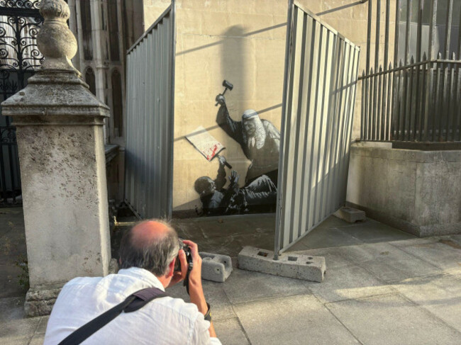 a-person-photographs-a-new-artwork-by-banksy-which-shows-a-judge-attacking-a-protester-with-a-gavel-at-the-royal-courts-of-justice-in-london-the-artwork-is-on-an-external-wall-of-the-queens-buildi