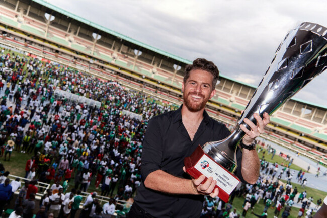 nairobi-kenya-25-jun-2023-johnathan-mckinstry-head-coach-gor-mahia-with-the-2022-23-kpl-league-winners-trophy-in-the-background-gor-mahia-fans-who-had-flooded-onto-to-the-pitch-following-the