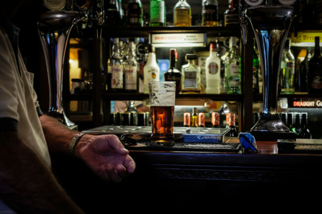 a-customer-sitting-with-his-half-empty-pint-of-beer-at-the-bar-of-a-traditional-pub-in-the-uk