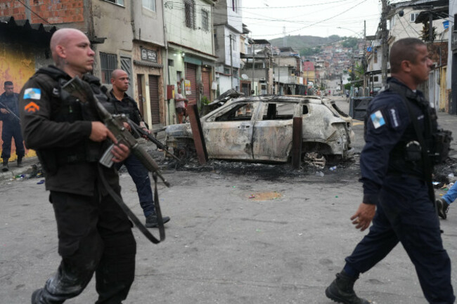 police-walk-past-a-burned-car-used-as-a-roadblock-during-a-police-operation-against-alleged-drug-traffickers-in-the-complexo-do-alemao-favela-where-the-criminal-organization-comando-vermelho-operate