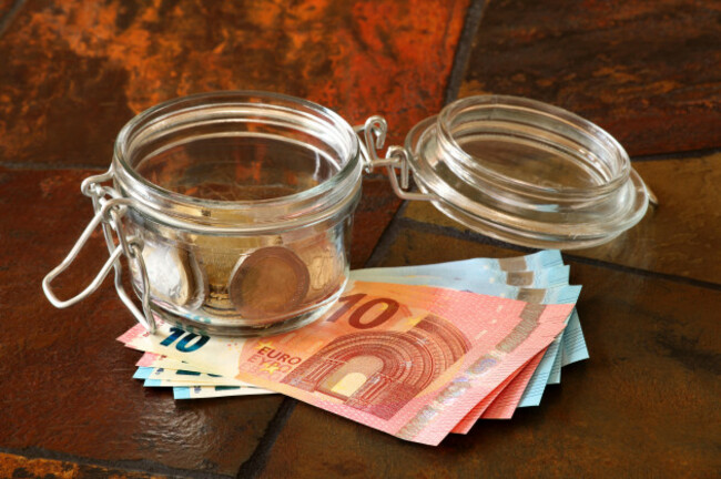 euro-coins-in-a-jar-with-euro-banknotes-underneath-shown-on-a-tiled-table-top