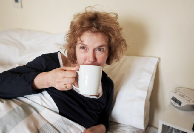 woman-looking-disheveled-drinking-cup-of-tea-after-waking-up-in-morning-in-bed