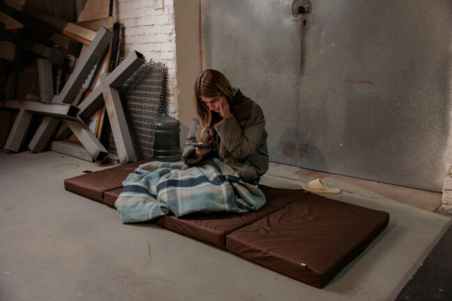 woman-reading-news-on-phone-in-bomb-shelter-war-in-ukraine-life-in-a-bomb-shelter-metro-station-woman-reading-news-on-mobile-phone